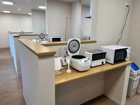 Dapur bersama asrama Oneness Court dengan rice cooker, microwave, dan peralatan masak